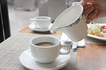 Pouring milk into coffee cup.