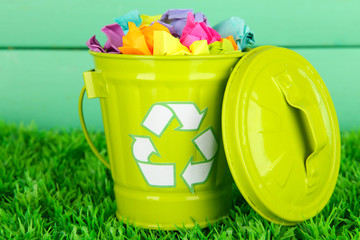 Fototapeta na wymiar Recycling bin on green grass on color wooden background