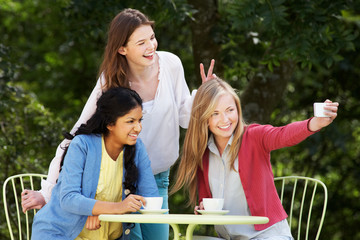 Teenage Girls Taking Photo On Mobile Phone At Outdoor cafe