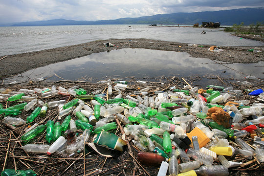 a pile of garbage and plastic bottles on the lake shore
