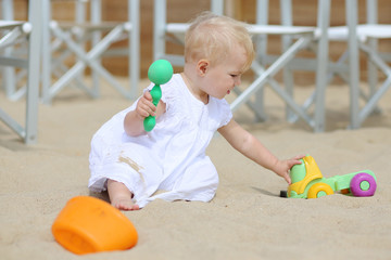 Active baby girl plays with toys sitting in sand on playground