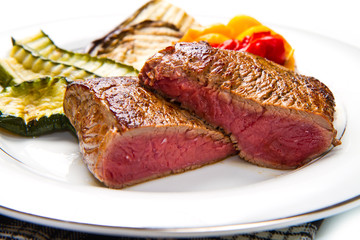 Delicious beef steaks on white dish with grilled vegetables