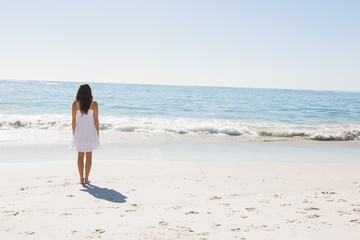 Fototapeta na wymiar Brunette in white sun dress walking to the sea
