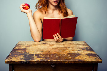 Naked woman reading and eating a peach