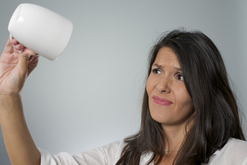 woman holds empty mug up side down with face expression