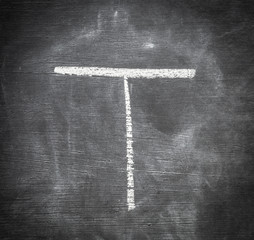 T - letter written on black chalkboard.