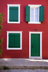 Fototapeta na wymiar Green shutters on a red wall, in Nafplio, Greece