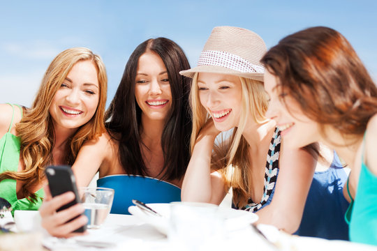 girls looking at smartphone in cafe on the beach