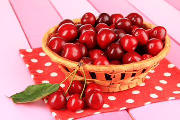 Cherry berries in wicker basket on wooden table close-up