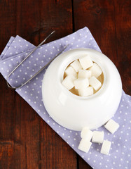Refined sugar in white sugar bowl on wooden background