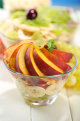 Tasty fruit salad in glass bowls, on white wooden table