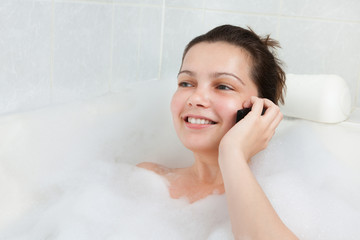 Young woman in bathtub talking on mobile