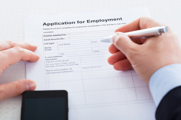 Close-up Of Hand Holding Pen Over Employment Application
