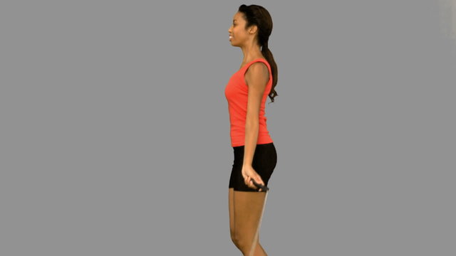 Pretty woman working out with a rope on grey screen