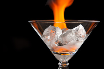 Ice cubes in glass with flame on shiny black surface