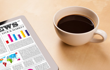 Tablet pc shows news on screen with a cup of coffee on a desk