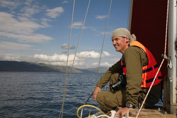 The smiling man in a life jacket sits on a nose of the yacht flo