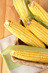 Crude corns in basket on napkin on wooden table