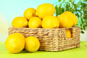 Ripe lemons in wicker basket on table on bright background