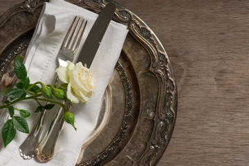 silver plate, fork and knife setting with white rose on wooden t