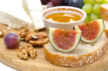 cheese, bread, figs, grapes, honey and nuts on a wooden board