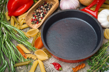 empty frying pan, vegetables and spices on wooden background