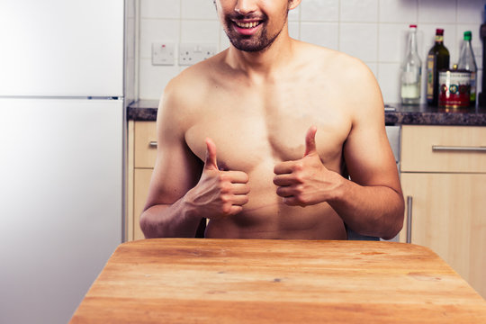 Naked young man in his kitchen giving thumbs up