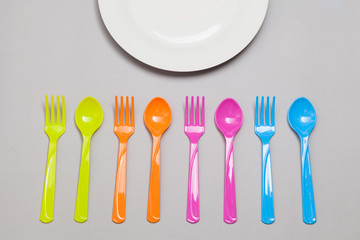 plastic spoon and fork on grey background with white dish