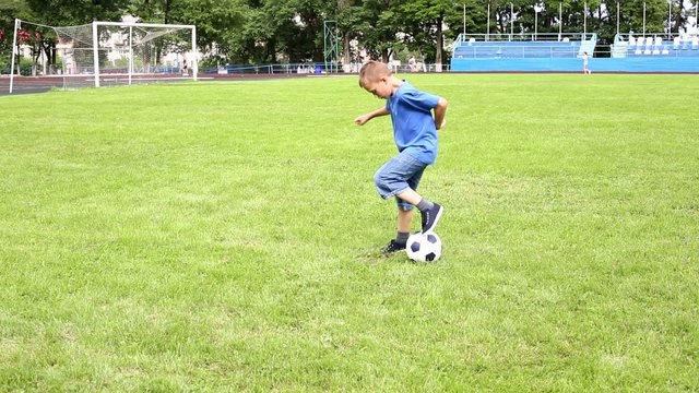 Boy plays soccer on a football field with natural grass.