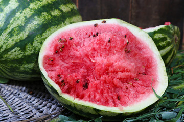 Ripe watermelons on wicker tray on grass near fence