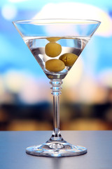 Martini with green olives on table in bar