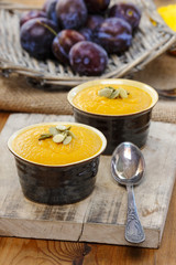 Creamy pumpkin dessert on wooden table. Raw plums in wicker bask