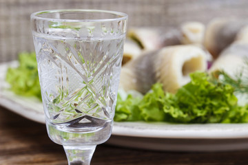 Glass of vodka and pickled herrings in the background.