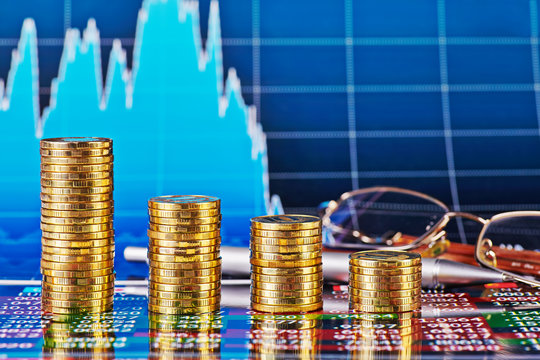Downtrend financial chart, glasses, pen and stacks of golden coi