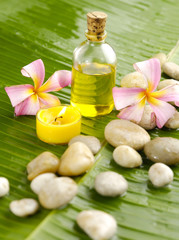 Obraz na płótnie Canvas Massage oil with candle and Plumeria and stones on banana leaf
