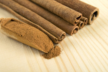 Cinnamon sticks and powder over wooden background close up