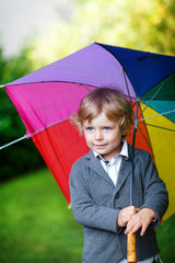 Little cute toddler boy with colorful umbrella and boots, outdoo
