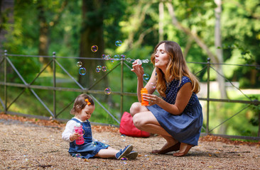 Beautiful mother and little daughter blowing soap bubbles in sum