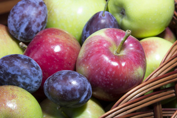 plums and apples in a wicker basket