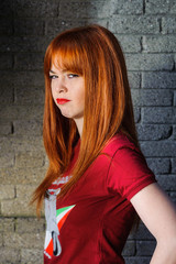 Red haired young girl looking angry in front of the wall