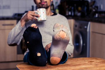 Man with worn out socks having coffee in kitchen