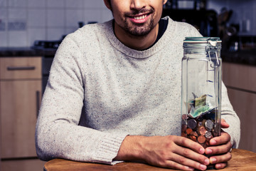 Happy man sitting in kitchen with piggy bank