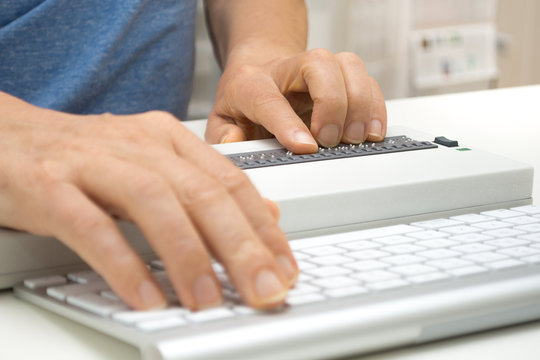Blind person working on computer with braille display, keyboa