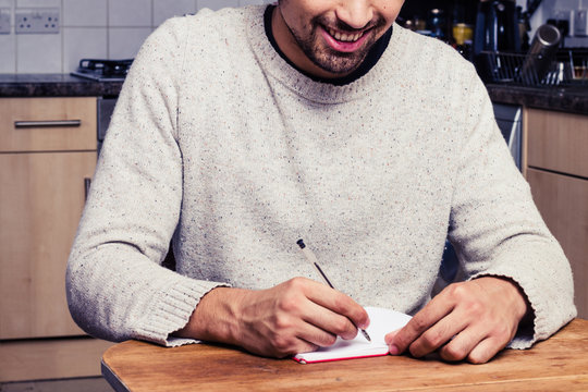 Smiling young man is writing in his kitchen