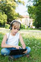 Boy is sitting on the grass in the headphones with your tablet