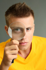 Fototapeta na wymiar Young man looking through magnifying glass on grey background