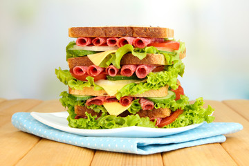 Huge sandwich on wooden table, on light background
