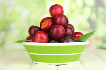 Ripe plums in bowl on wooden table on natural background