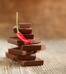 Red chili pepper on stack of dark chocolate pieces on wooden bac
