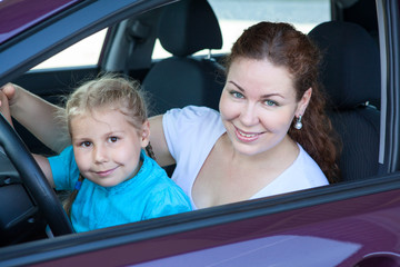 Happy mother with small daughter sitting together on driver seat